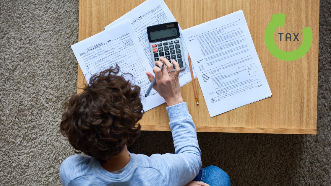 Person sitzt am Tisch mit Steuerunterlagen und Taschenrechner, arbeitet an der Steuererklärung