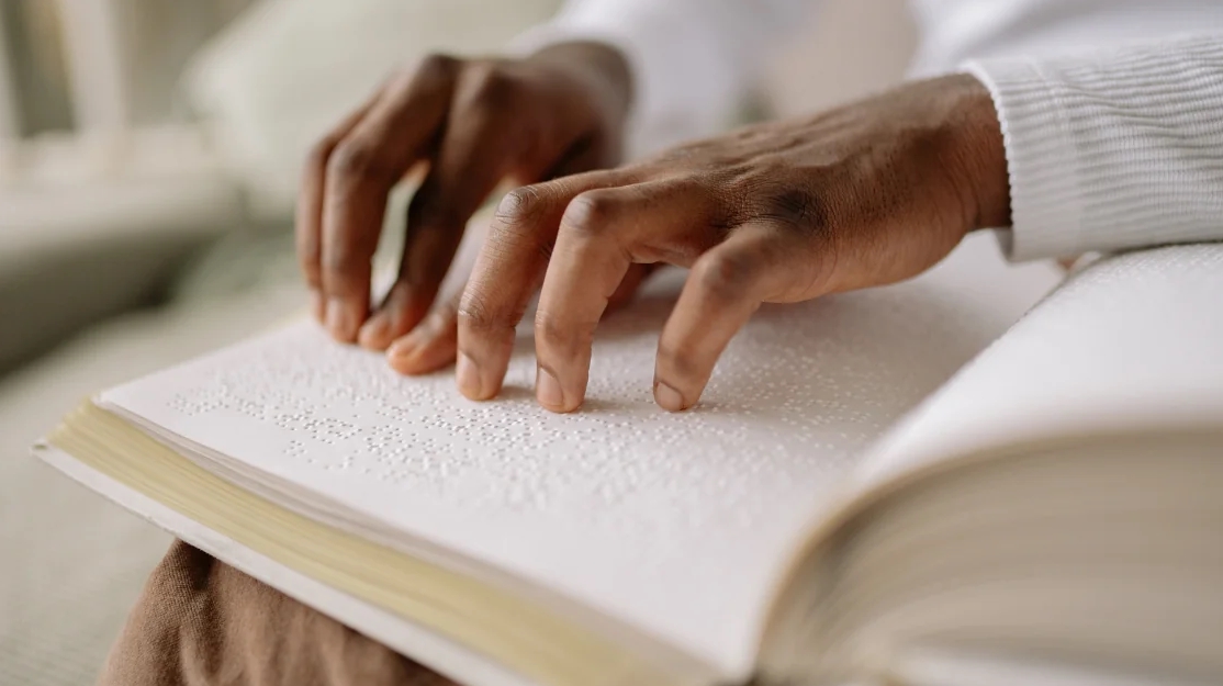 Nahaufnahme von Händen, die über ein Buch in Blindenschrift (Braille) tasten – Symbol für Sehbehinderung