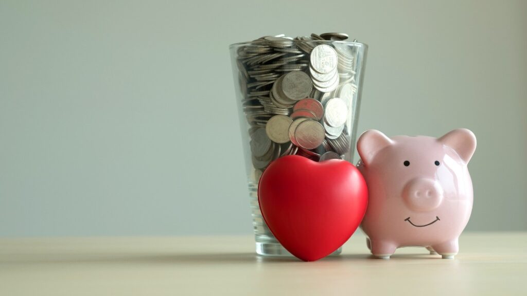 Glas mit Münzen, rotes Herz und rosa Sparschwein symbolisieren Altersvorsorge, Gesundheit und finanzielle Sicherheit
